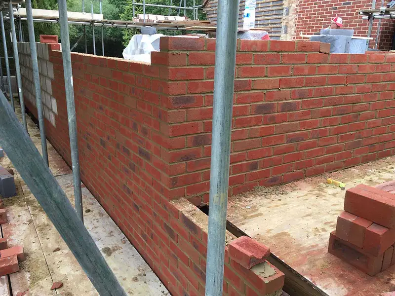 Bricklayers in hi-vis building the facing brick walls of an extension from scaffolding