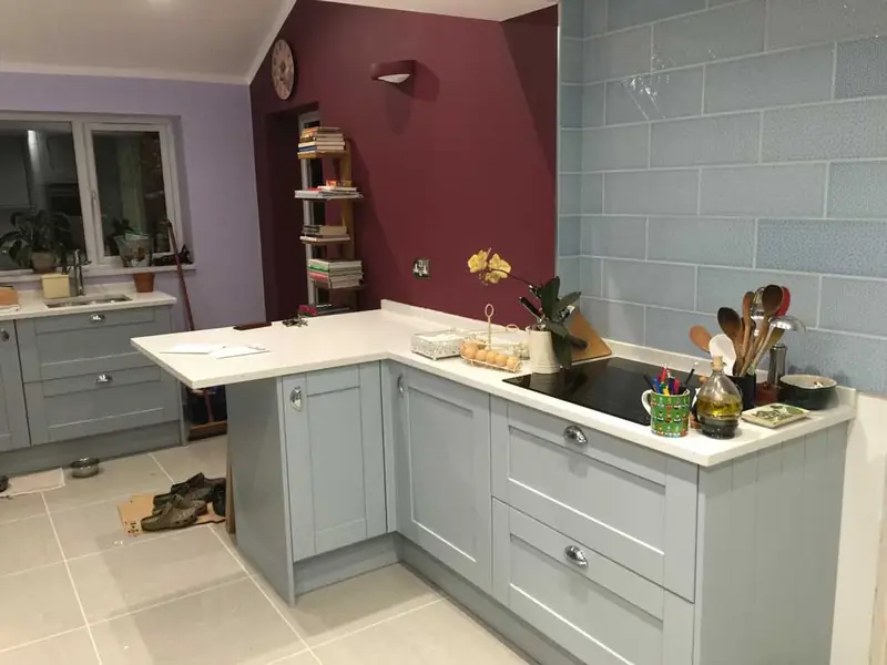 Grey shaker-style kitchen with white worktops and a burgundy feature wall, in a house in Fulmer