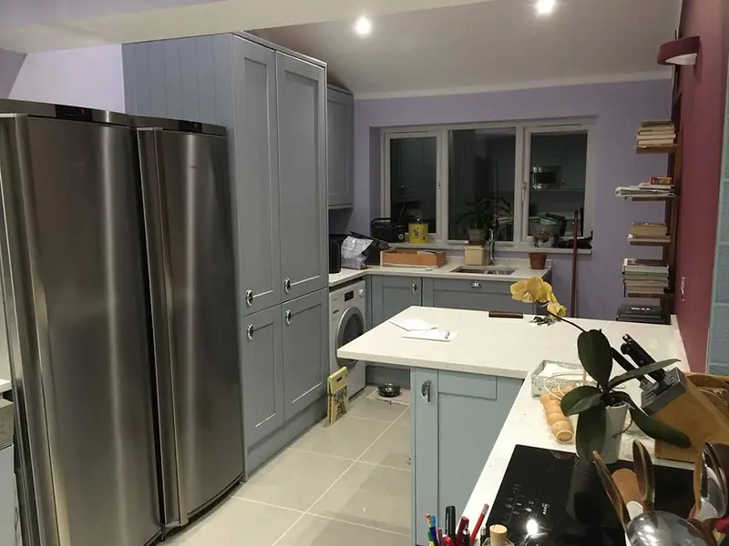 Grey shaker-style kitchen units with a tall fridge, white worktops and a sink under the window