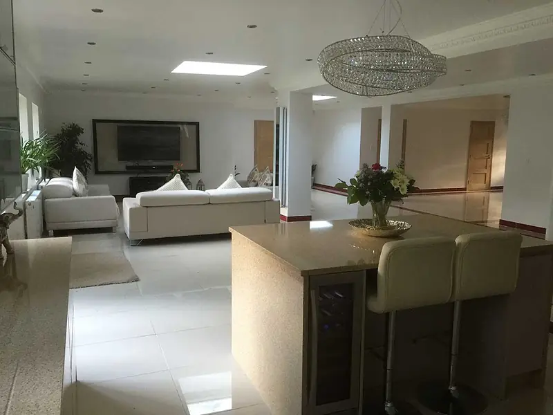 Open-plan kitchen with a stone-topped island and bar stools, opening onto a large living area