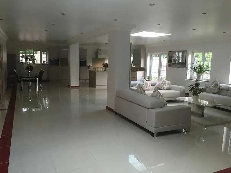 Large open-plan living and dining space with white tiled floors, rooflights and pale sofas