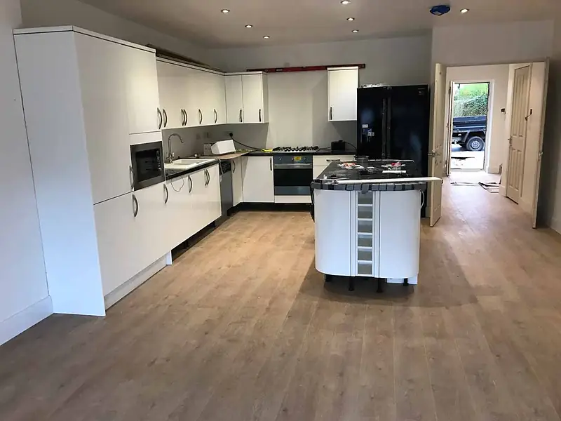 Newly fitted kitchen with white units, an island with a dark worktop and wood-effect flooring